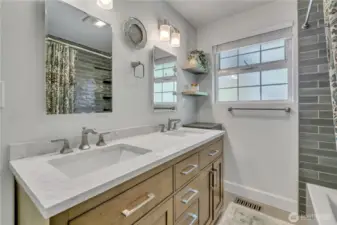 Updated full bath with dual-sink vanity, quartz counters, and sleek gray subway tile surround.