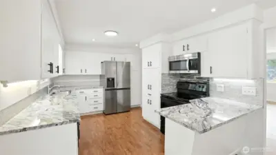 Updated kitchen that features newer grab handles, tile backsplash, light fixtures, laminate flooring, and appliances.
