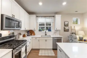 The open kitchen and has stainless appliances, gas stove, quartz counters, tile backsplash and tons of counter and cupboard space.
