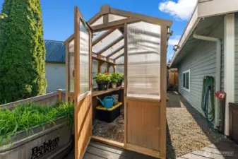 There is a garden shed and raised garden beds behind the green house.