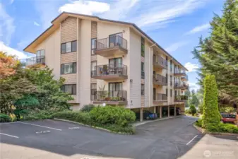 A view of the condo building surrounded by gardens and the view of the water. Your reserved parking is the first covered one immediately left