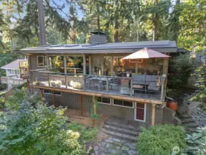 Mid-century inspired exterior with expansive upper deck, contemporary railings & private forest setting.