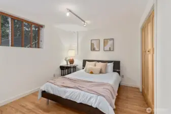 Bright secondary bedroom with hardwood floors & windows framing forest views.