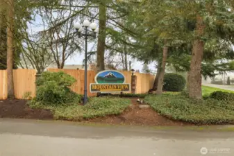 Welcoming entrance to this well-maintained community, framed by mature trees and lush landscaping, creating a warm first impression as you arrive home.