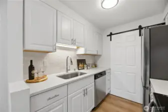 The kitchen features all-new cabinetry, quartz countertops, and a designer backsplash, while the laundry closet is thoughtfully enclosed with a stylish barn door feature.