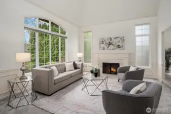 The elegant formal living room impresses with soaring vaulted ceilings, a wall of arched windows flooding the space with natural light, and a classic fireplace framed by timeless millwork and wainscoting.