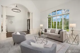 Dramatic arched ceilings, elegant columns, and a stunning floor-to-ceiling arched window flood this formal living room with natural light, offering a seamless view of the lush mature landscaping.