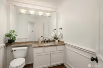 The elegant powder bath features a classic vanity with quartz counters, wainscoting, and refined finishes, a polished and welcoming space for guests on the main level.