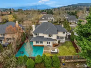 This stunning aerial view showcases the home's impressive footprint, sports court, spacious yard, and three-car garage, all nestled among lush mature landscaping in the heart of the sought-after Trossachs community.