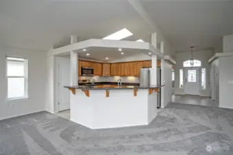 From the open living area, you can see into the kitchen, which features a convenient eating bar—perfect for guests to gather or for enjoying a quick snack. Natural light pours in through the skylights, brightening the entire space.