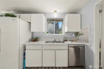 Window over the double-bowl sink brings in natural light; tile counters and upper/lower cabinets keep essentials organized.
