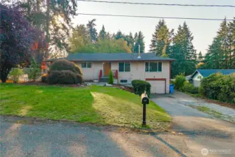Street view showcases the home’s generous front yard and quiet setting. The well-maintained lawn and mature trees provide a sense of privacy while maintaining a friendly neighborhood feel.