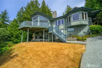 Expansive wraparound deck and soaring windows highlight the home's architectural charm and stunning setting amidst lush evergreens, overlooking Puget Sound.