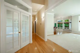 View down the hall toward the Primary Bedroom. Office on the left, living room to the right. Kitchen and dining area in the background. Bedroom 1 & 2 behind the photographer.
