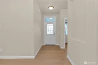Entry way looking back to designer front door with decorative transom glass inlay showcases hallway niche and hardwood floors.