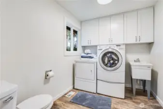 Back to the main level, the laundry room leads to the garage. Above the washer and dryer are new white cupboards. Also featured is a new toilet and utility sink.