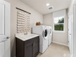 Utility room with sink, and an additional dor leading into primary closet. Photo is representational. Actual home is under construction and finishes and colors will vary. See site agent for details.