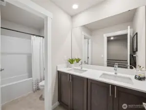 Hall bath with double sink vanity.  Notice the door separating the sink and the shower to allow multiple people to get ready for the day. Photo is representational. Actual home is under construction and finishes and colors will vary. See site agent for details.