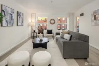 A charming living area with flexible seating options. Two large windows bring natural light into the room.