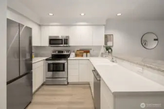 A crisp and modern kitchen with clean lines, white on white cabinetry and countertops that open to the living area for a more spacious feel.