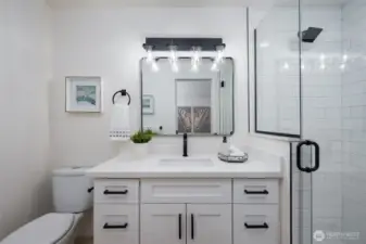 Updated bathroom showcasing a new vanity, stylish mirrors and lighting, plus a tiled shower with a sleek glass door.