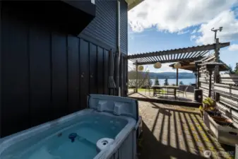 Private and fenced side yard opens to views from the included hot tub. A pergola used for dining and entertaining is seen in the background.
