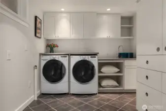 A second laundry room includes an oversized Kenmore Elite washer and dryer, ample cabinetry, a Liebherr refrigerator, and a built-in ironing board to streamline everyday living.