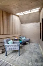 A private covered sitting space off the entryway with skylights and a paver patio.