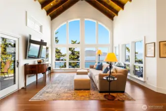 As evening falls, the family room transforms with a warm glow while the windows frame shifting skies and reflections across the water.