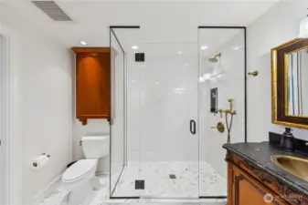 A Carrara marble bath finished with a frameless glass shower, brass fixtures, and a custom carved vanity blends classic materials with modern design.