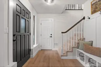 Bright, open ground-floor entryway with garage access, storage bench, and stairs leading up.
