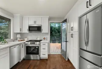 Bright, open kitchen featuring brand-new stainless steel appliances, sleek cabinetry extending to the ceiling, and an inviting breakfast bar—perfect for entertaining, casual dining, and gathering with friends.