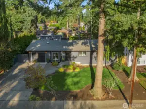 This listing features a spacious lot with lush landscaping, mature trees, and a paved driveway.