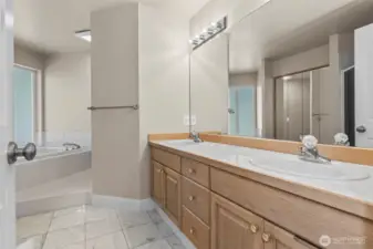 Primary bath with dual vanities, luxury flooring, walk-in closet, and soak tub