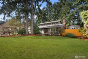 Expansive front yard with manicured lawn, mature evergreen trees, and landscaped garden beds leading to the covered front entry of this two-story Puyallup home.