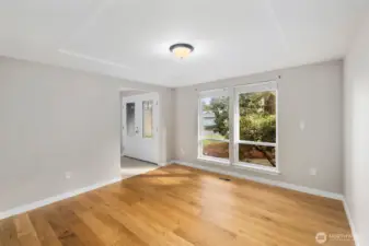Light-filled front room with large windows, tray ceiling detail, and warm hardwood flooring near the home’s main entry.