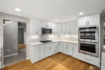 Updated kitchen with white cabinetry, double wall ovens, modern tile backsplash, and generous counter space.