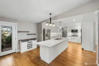 Bright kitchen with oversized island, pendant lighting, stainless steel appliances, and adjacent dining space with backyard access.