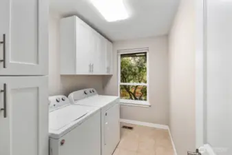 Dedicated laundry room with washer and dryer, upper storage cabinets, and window bringing in natural light.