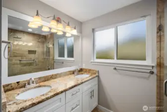Primary bathroom with double vanity, large mirror, updated lighting, and walk-in tile shower.
