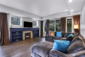 Cozy living room with a custom built fireplace surround and large windows showcasing the greenery outside.