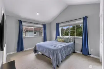 Bright primary bedroom with vaulted ceilings and large windows that offer peaceful views of the treetops.