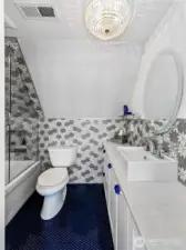 With a cascade of daisy tile, deep blue penny floor, and a crystal chandelier overhead, the upstairs bath offers both whimsy and refinement—tucked under the eaves like a secret spa.