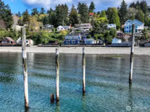 From the water, the home reveals itself like a secret—nestled among Browns Point’s hillside cottages and framed by weathered pilings, the last remnants of the old Mosquito Fleet dock that once connected these shores to the greater Sound. With its bold blue façade and cheerful yellow door, the home stands as a beacon of character and calm, its terraces cascading toward the tide like steps in a well-kept promise.