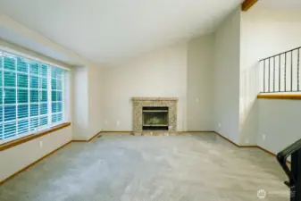 Spacious split-level living area featuring vaulted ceilings, exposed wood beams, and an open railing overlooking the kitchen. Soft carpet, durable tile flooring, and abundant natural light create a warm, functional layout with easy flow between levels—ideal for flexible living and entertaining.