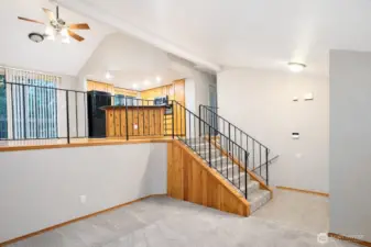 Spacious split-level living area featuring vaulted ceilings, exposed wood beams, and an open railing overlooking the kitchen. Soft carpet, durable tile flooring, and abundant natural light create a warm, functional layout with easy flow between levels—ideal for flexible living and entertaining.