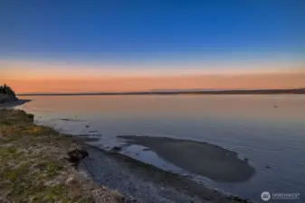 Sunset over the water casts vibrant colors across the sky and bay.