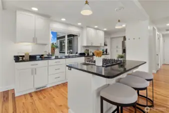 Lots of cabinet storage, island seating for three, gas cooktop, and sink with great serene outlook to the backyard. The hallway on the right leads to the main floor bedrooms and off to the left is the bonus room.