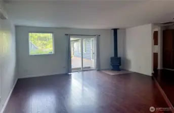 Large living room next to entry hallway with wood burning fireplace and doors leading out onto deck