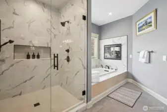 Indulge in everyday serenity within this spa-style ensuite, where an oversized glass-enclosed shower with dual showerheads meets a jetted soaking tub framed by porcelain marble tile. A double-sided gas fireplace adds ambiance from both the bath and bedroom, elevating relaxation with a warm, luxurious glow. Soft natural light and sophisticated finishes invite you to linger a little longer.